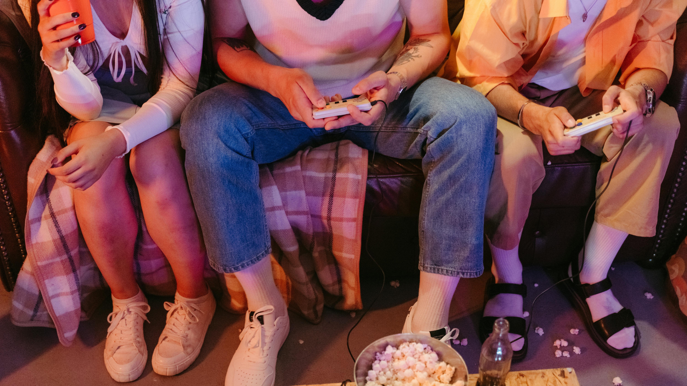 Group of friends enjoying gaming session using discount game controllers while sitting on a couch with snacks